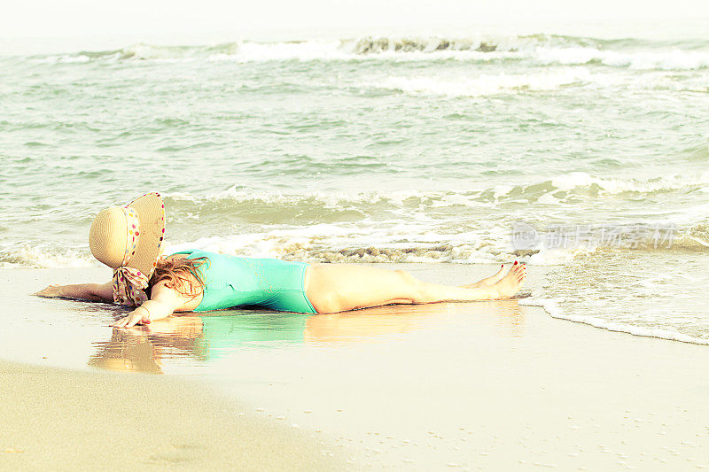 年轻女子戴着草帽躺在海滩上