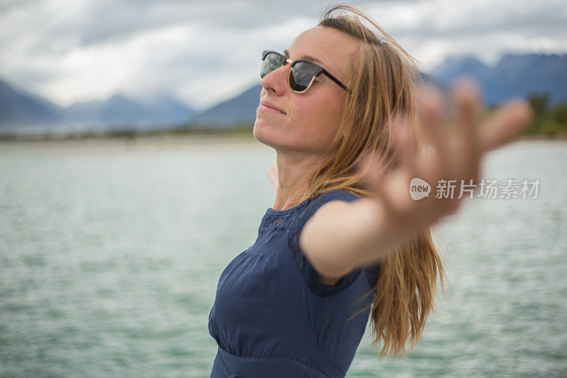 一位兴高采烈的年轻女子站在湖边，张开双臂，新西兰