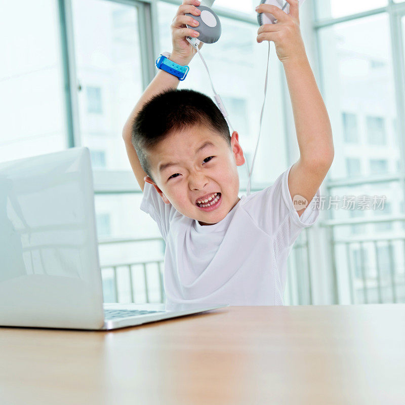 年轻的亚洲男孩戴着耳机使用笔记本电脑