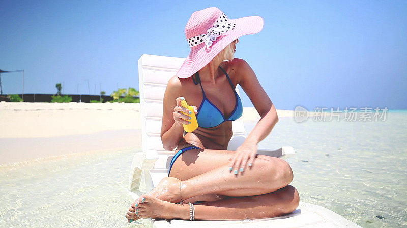 一名金发女子坐在马尔代夫的浅水中，涂抹日光浴霜