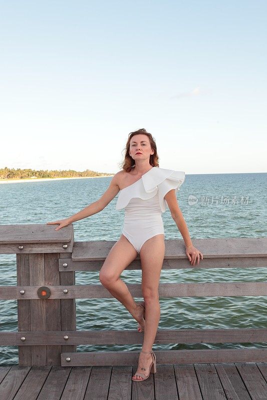 年轻女子站在一件白色泳衣前的大海。