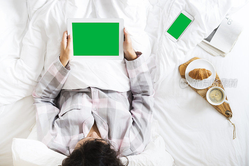 年轻女子在床上使用绿色屏幕的电子平板电脑