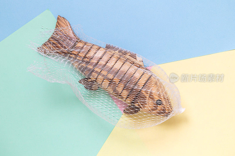 鱼玩具被捕获在渔网孤立在粉彩背景极简抽象的概念。