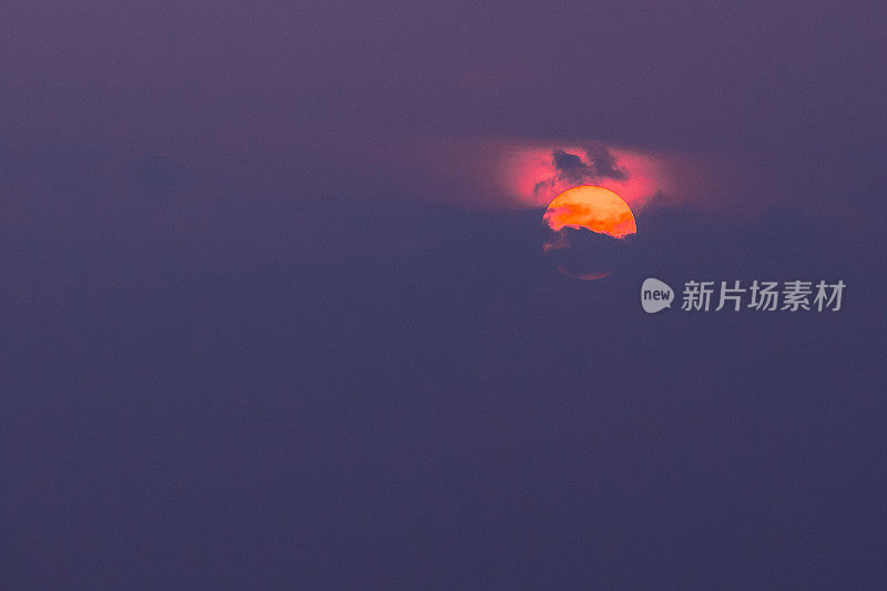近距离观察橙色的太阳盘部分覆盖的云与深红色辉光顶部，紫色的天空背景
