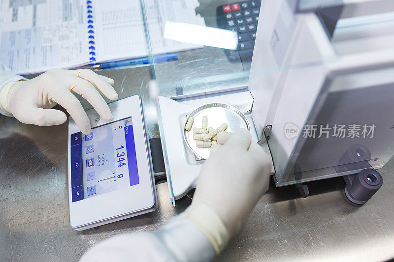 实验室工作人员戴着无菌橡胶手套，在控制秤上称生产好的药片。