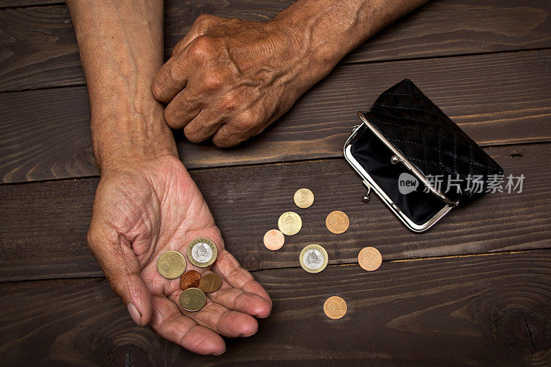 贫困。一个老人把硬币放在空空的旧皮夹上。退休后贫困的概念。