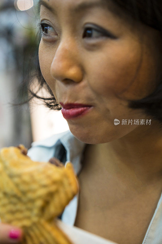 日本京都，一名妇女在街上吃Taiyaki。