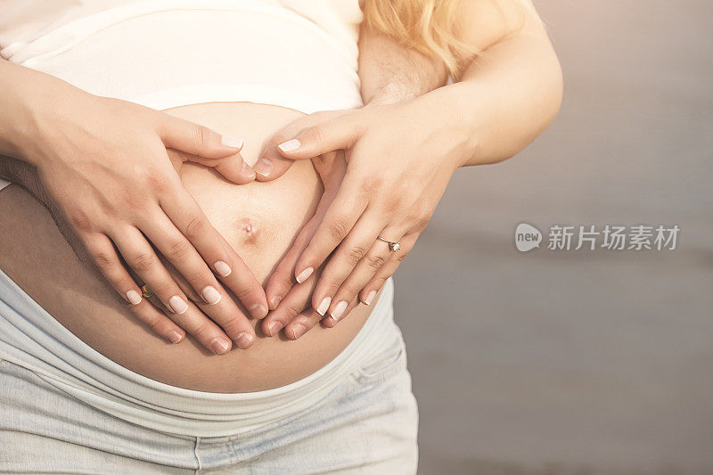 一对怀孕的夫妇把他们的手放在肚子上做成心形
