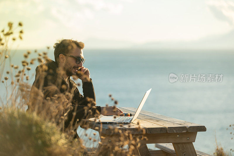 年轻的商人坐在大自然的木桌边用笔记本电脑工作