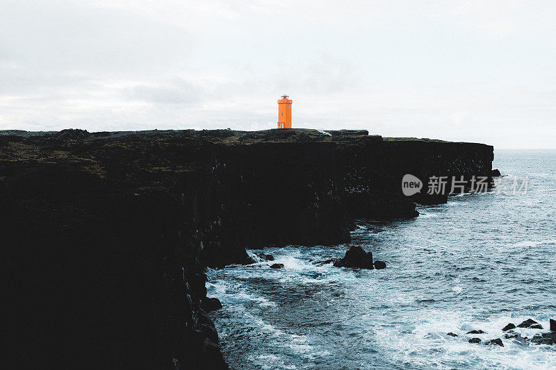 在冰岛，日出时暴风雨海面上的橙色灯塔