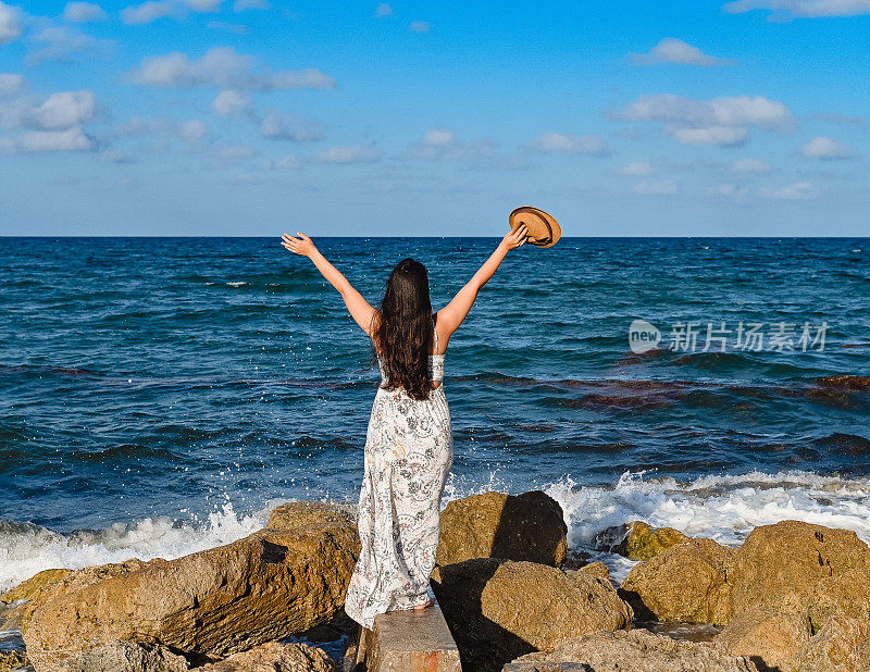 年轻漂亮的泰国裔柬埔寨裔美国妇女站在海边一块露出海面的岩石上