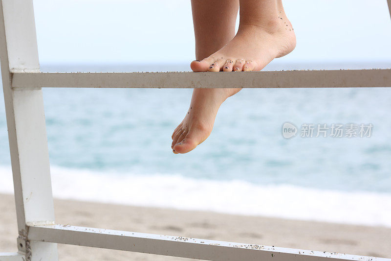 年轻女子光着脚爬上了沙滩上的梯子