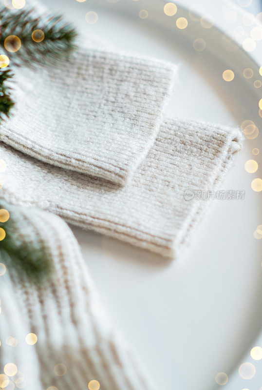 折叠针织米白色羊毛衫小松果绿色杜松枝金色灯花环在木板木桌子靠窗。舒适的冬夜。新年圣诞魔幻气氛。Scandi风格