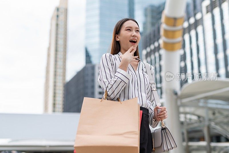 迷人聪明的亚洲女商人雇员在曼谷市中心商业区疯狂购物后，看到另一个狂欢节销售，她笑得很开心