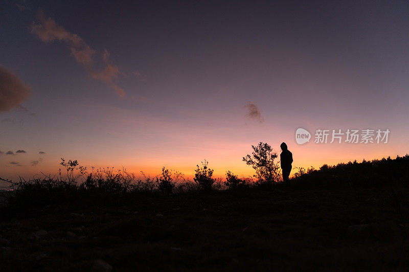 黄昏时一个人走在山顶上的剪影，面对着红色的天空和夕阳