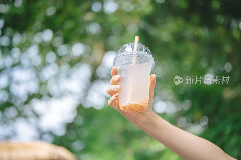 手持果汁可回收的塑料果汁杯和可回收的纸吸管，保持户外的绿色自然背景