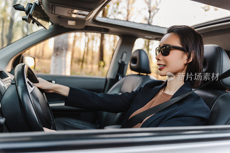 亚洲女人开着车，面带微笑。一个年轻成功快乐的女人正在开车。