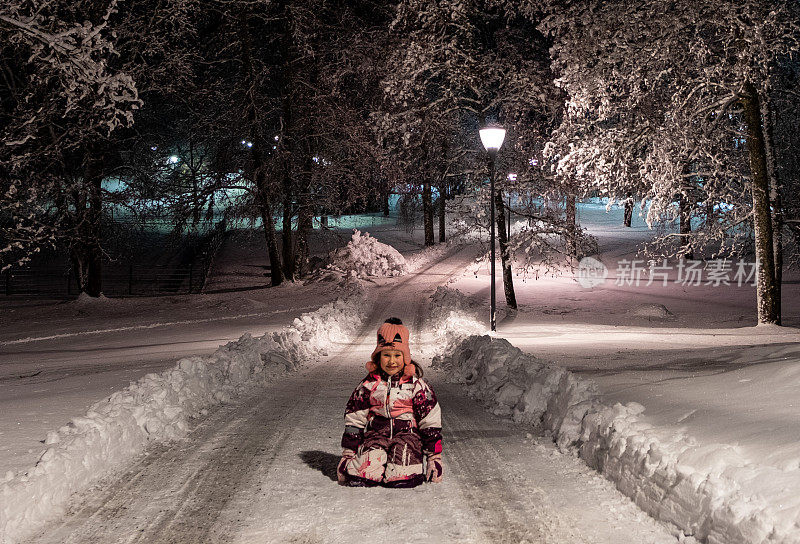 7岁的小女孩在冬天的大街上。孩子调皮地在公园里，坐在马路上，放假到深夜。