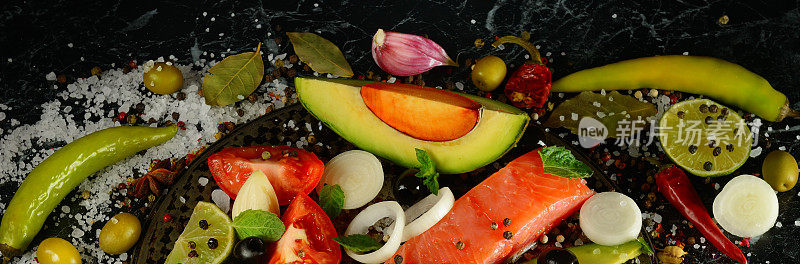 粉红色的三文鱼片，香料和蔬菜，黑色的背景。宽的照片。