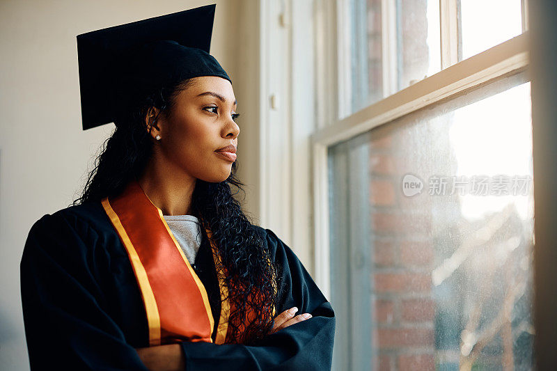 一位身着毕业礼服的非裔美国妇女凝视着窗外。