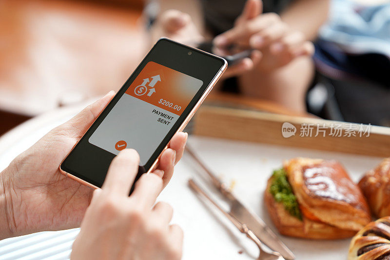 两个朋友在咖啡馆用餐时，用智能手机上的数字钱包分摊账单，收发账单。