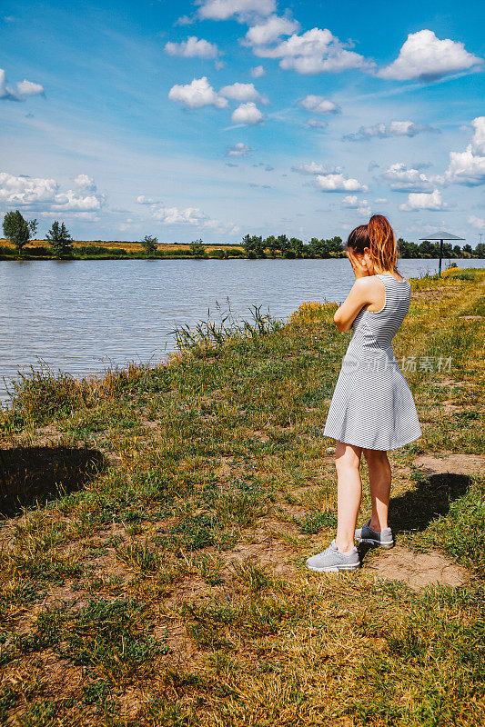 十几岁的女孩穿着夏装，双手捂着脸站在河岸上