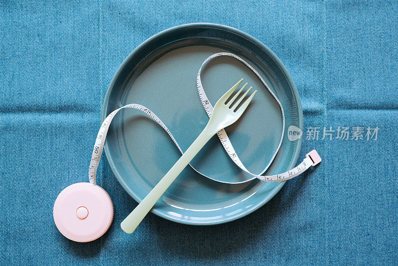 空的海军蓝陶瓷盘与叉和卷尺在蓝色织物表背景。健康饮食理念。俯视图