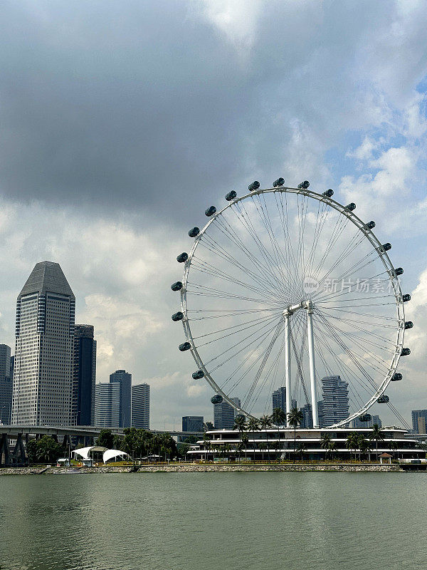 新加坡摩天轮的特写图像，以阳光明媚，多云的蓝天为背景，城市海滨景观，摩天大楼，重点在前景
