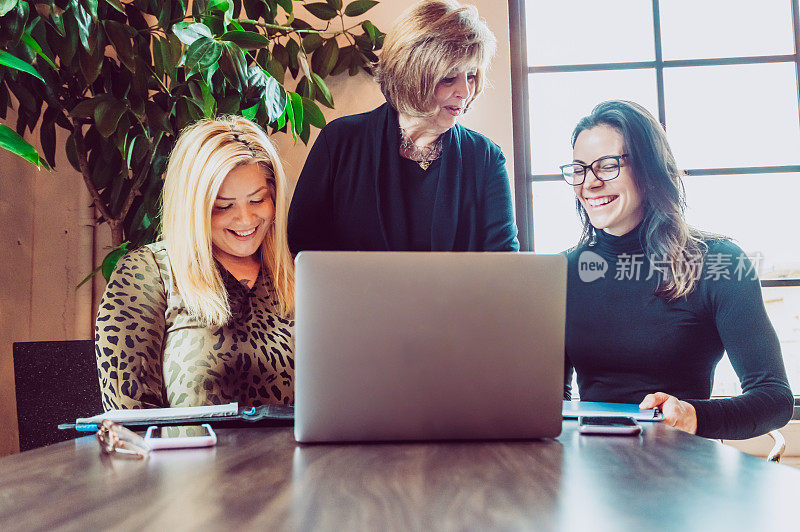 工作中的女性，会议桌旁拿着笔记本电脑的三位女企业家，商业伙伴、同事或客户和代理商