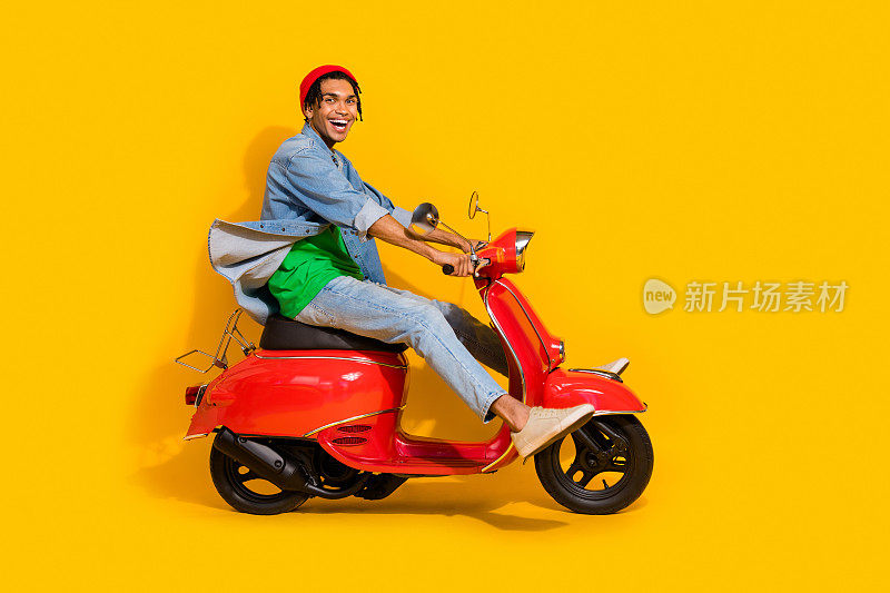 漂亮的年轻人的全尺寸照片驾驶红色老式摩托车助动车兴奋穿着时髦的牛仔裤装孤立的黄色背景