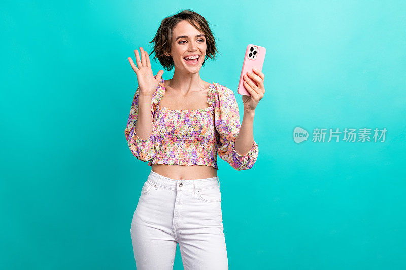 肖像积极的女孩与鲍勃发型穿着印花衬衫在智能手机视频通话孤立的蓝绿色背景