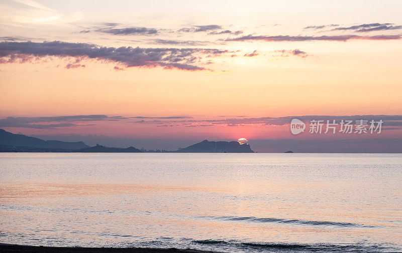 明亮的日出掠过海面，一座山在朦胧的背景中。圣胡安海滩阿利坎特