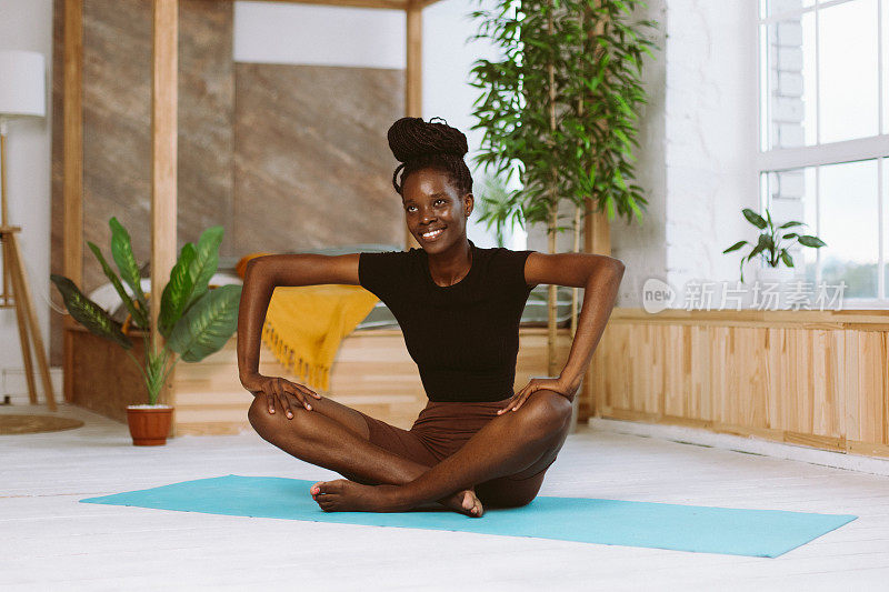 美丽和运动的非洲女人微笑着坐在蝴蝶姿势，在装饰的工作室体操垫上做瑜伽。肌肉伸展，体操练习，健身，保持身体健康