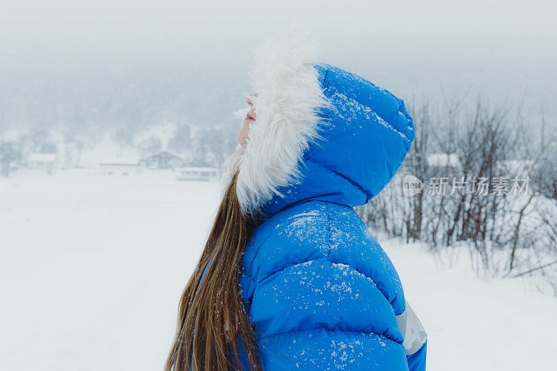 在大雪中漫步在斯堪的纳维亚村庄的蓝大衣女子欣赏冬天的童话