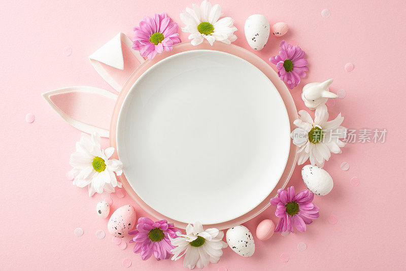 喜庆的复活节用餐概念。从盘子里往外看的兔耳朵，周围是彩绘的鸡蛋、陶瓷兔子、菊花和红色背景上的五彩纸屑，为文字留出空间