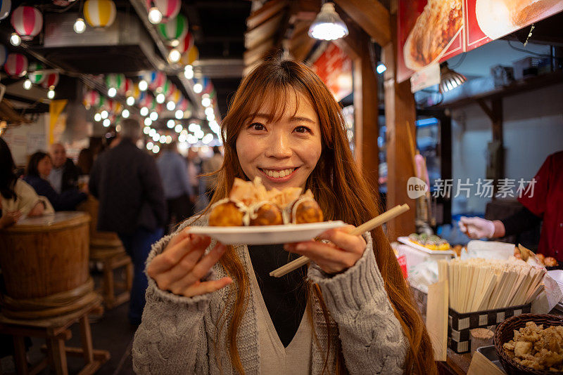 在日本居酒屋风格的美食广场，女游客手持章鱼烧的肖像