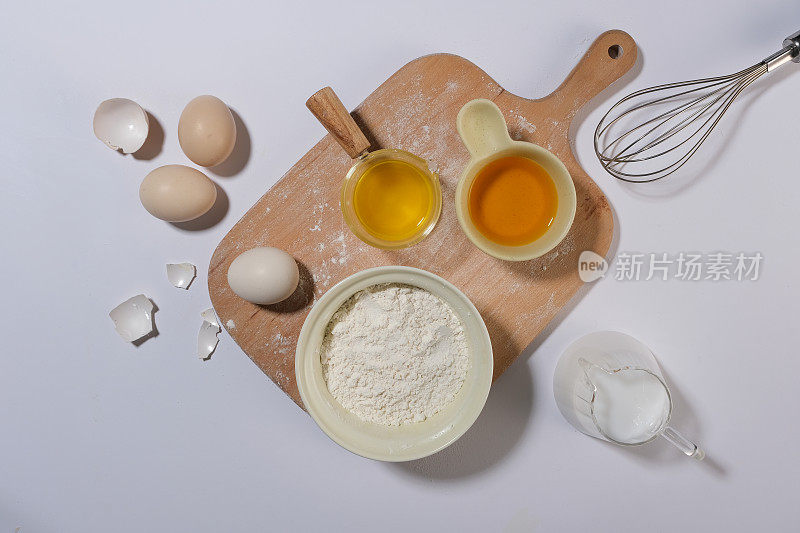 俯视图的烤蛋糕或糕点的材料和器具有足够的鸡蛋，面粉，牛奶，打蛋器和木托盘在中间。用来展示烹饪或烘焙产品的空白空间