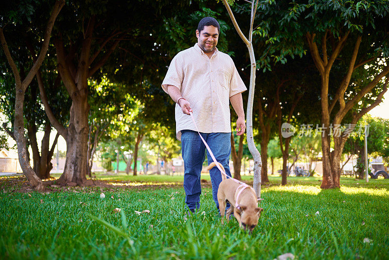 一个拉丁男人带着他的狗在公园里散步