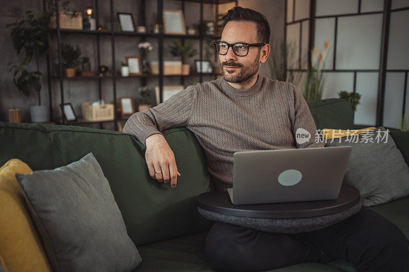 年轻英俊的男性自由职业者在家里舒舒服服地坐在沙发上用笔记本电脑工作