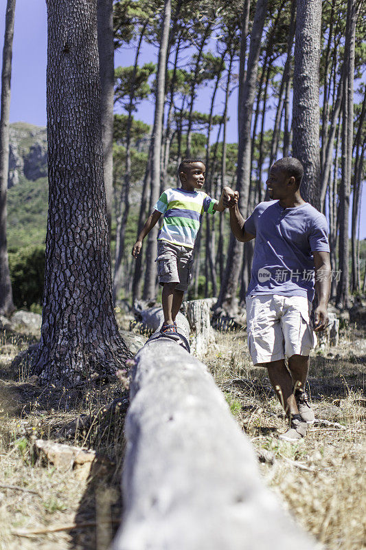 一位非洲父亲帮助儿子在圆木上行走