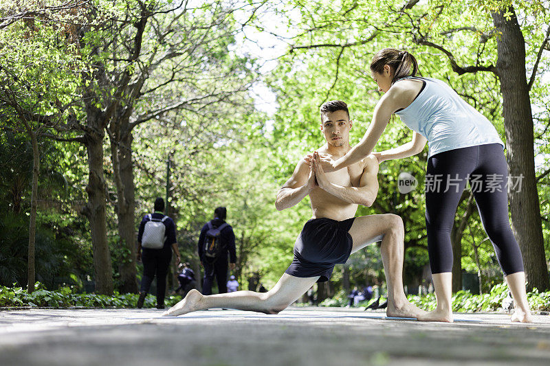 女瑜伽教练在公园里帮助她的男学生