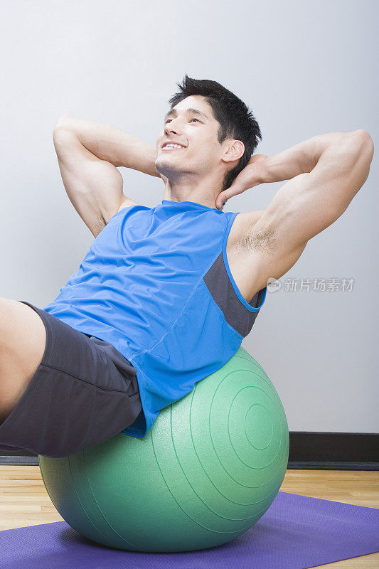 一个年轻人在健身房的健身球上做仰卧起坐