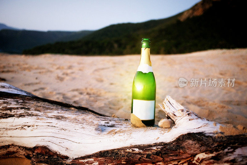 日落海滩上的空香槟瓶和浮木