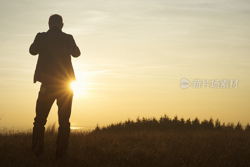 一个人站在那里用手机拍日落