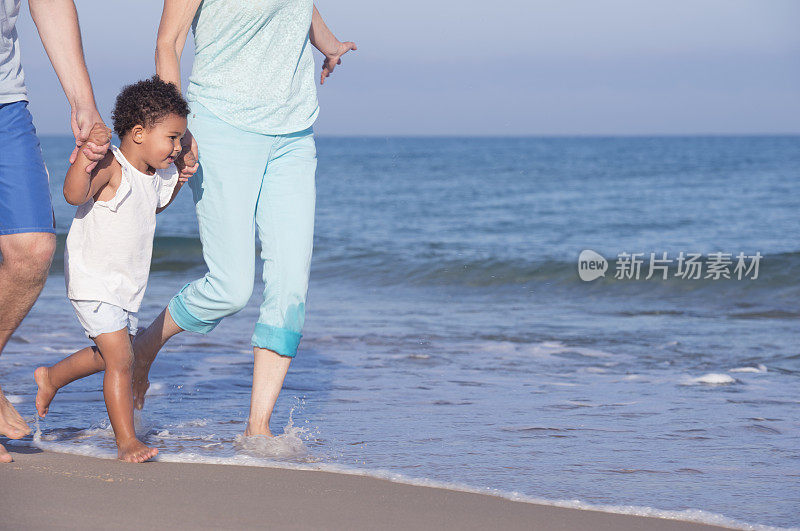 孩子牵着父母的手在沙滩上奔跑。