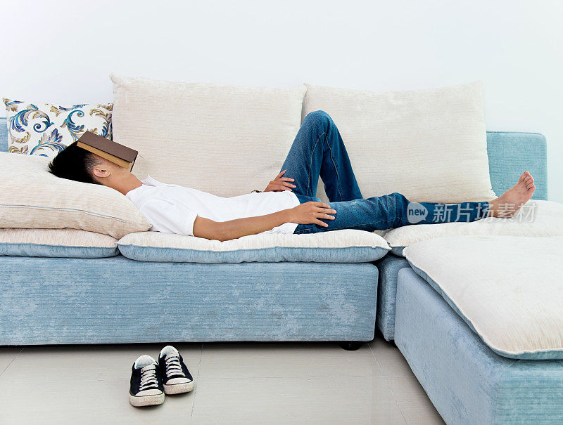 年轻人睡在沙发上，脸被书遮住了