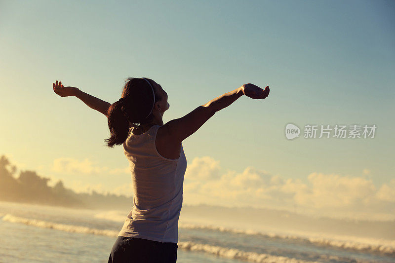 年轻健康的生活方式年轻女子在日出的海边海滩张开双臂