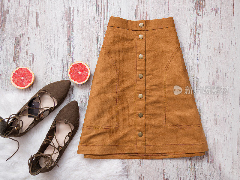 棕色麂皮裙，棕色麂皮鞋，切成两半的葡萄柚。木制背景。时尚的概念。俯视图
