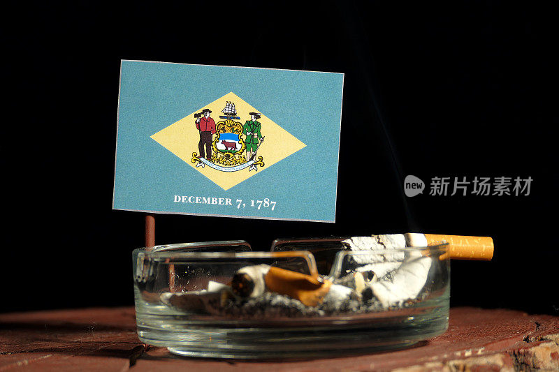 特拉华国旗和燃烧的香烟在烟灰缸孤立的黑色背景