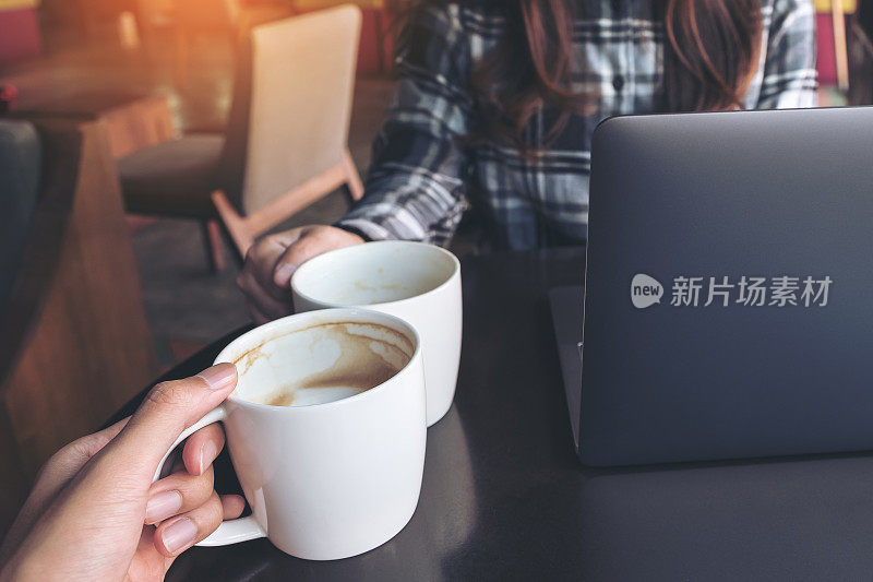 近距离拍摄的两个人在咖啡馆用笔记本电脑工作时碰杯喝白咖啡